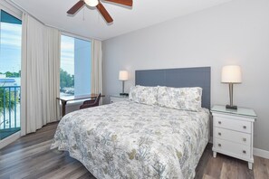 A bedroom with a bed, nightstands, a desk, and a view through a large window.