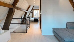 Un dormitorio en el ático con techo inclinado, vigas de madera, una cama y un sofá.