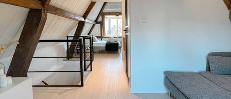 An attic bedroom with a sloped ceiling, wooden beams, a bed, and a sofa.