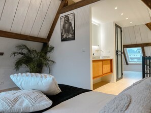 A bedroom with a bed, pillows, a plant, and a view of a kitchen and balcony. - The heritage harbour loft (Dordrecht)