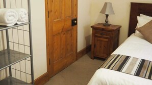 Une chambre à coucher avec un lit, une table de chevet, une porte en bois et une étagère en métal où sont posées des serviettes.