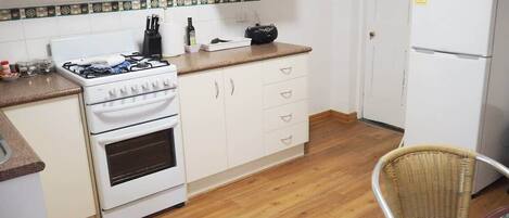 A kitchen with a stove, microwave, refrigerator, and a wicker chair.