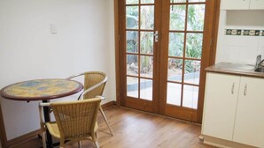 Une pièce comprenant une table à manger et des chaises, un coin cuisine avec des placards et une grande porte vitrée donnant sur un espace extérieur.