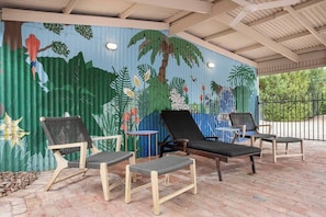 A covered outdoor seating area with lounge chairs and a mural of tropical foliage.