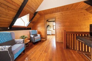 A cozy attic room with wooden walls and a sloped ceiling. It features two patterned sofas, a small table with a plant, and a wooden railing. - Willunga Cottage- Sleeps 6, Pool (Willunga)