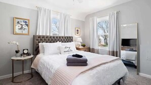 A bedroom with a large bed, a bedside table, a nightstand, a ceiling fan, and a window with curtains. - Pet-Friendly 3BR South Euclid Home | Patio + Yard (South Euclid)