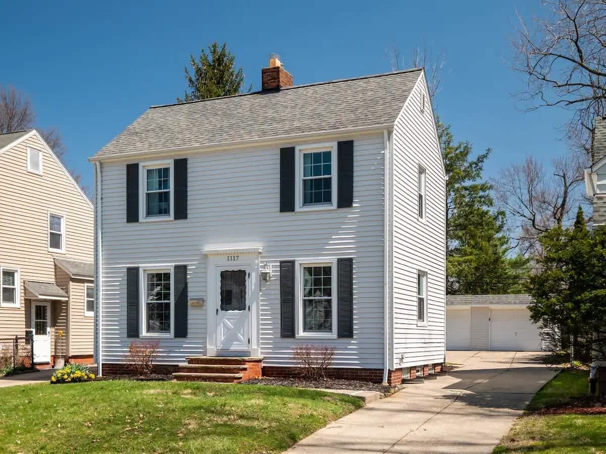 A two-story white house with black shutters, a front porch, and a garage.