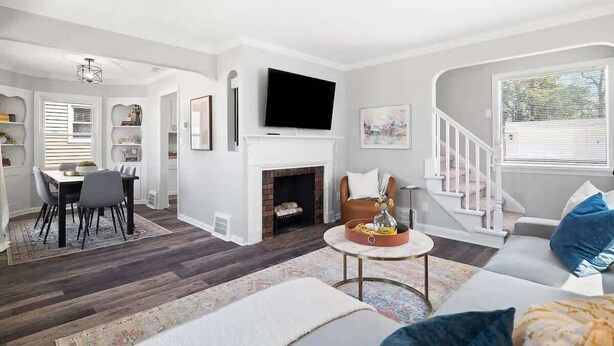 A modern living room with a fireplace, a dining area, and a staircase leading to another level. - Pet-Friendly 3BR South Euclid Home | Patio + Yard (South Euclid)