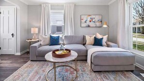 A living room with a grey sectional sofa, a round coffee table, and a patterned rug. - Pet-Friendly 3BR South Euclid Home | Patio + Yard (South Euclid)