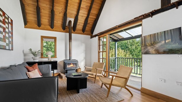 A cozy living room with a fireplace, a sofa, a chair, and a large window with a view of trees. - 'Old Alloway'- 7 Bedrooms/ Sleeps 17 -9mins to CBD (Eglinton)