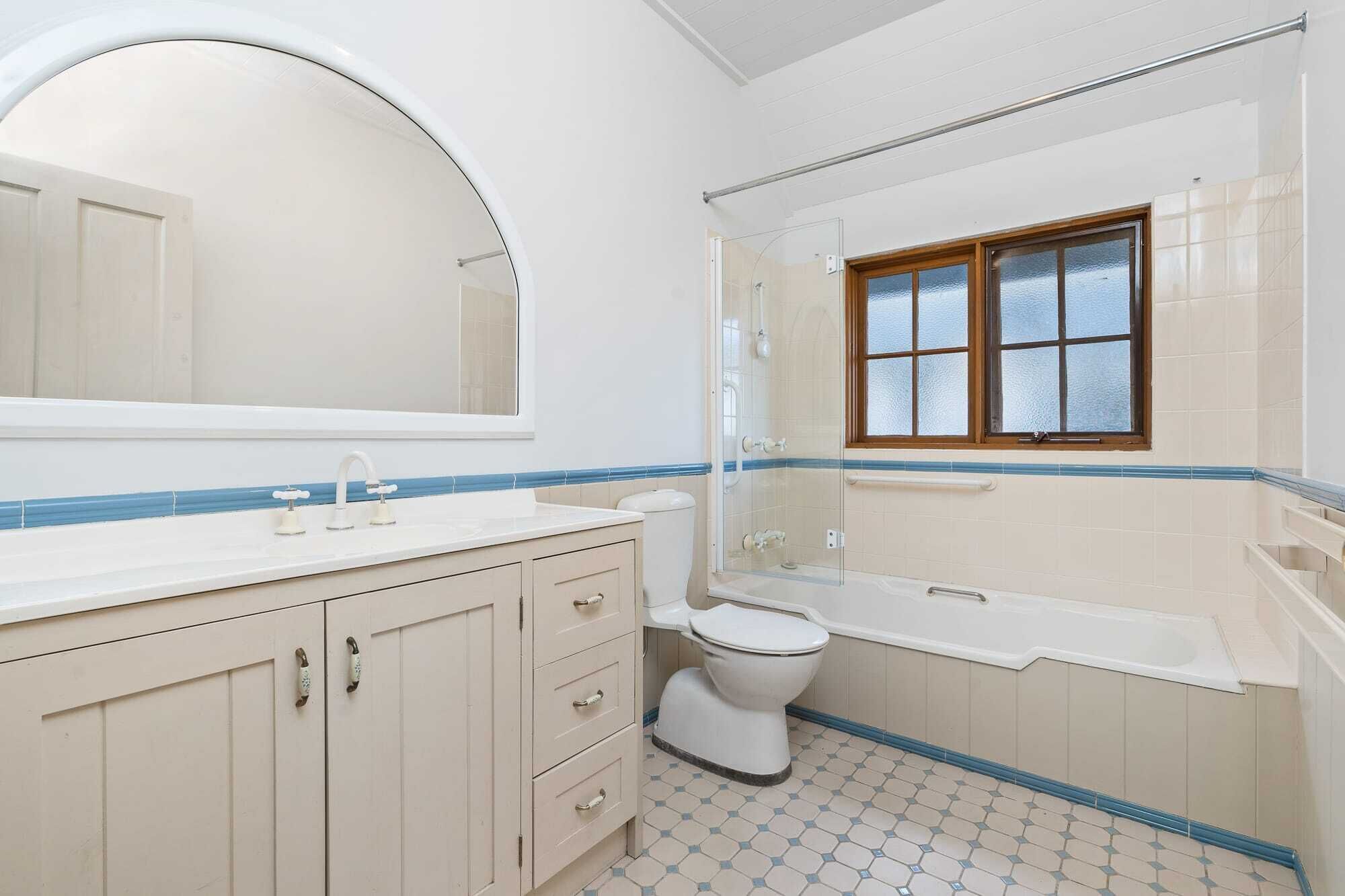A bathroom with a large mirror, a toilet, a shower, and a window.