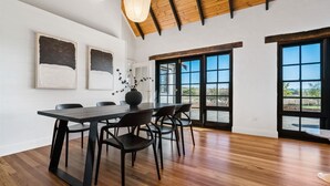 A dining area with a wooden table, black chairs, and a vase with dried flowers. There are three framed abstract paintings on the wall, and large windows with a view of the outdoors. - 'Old Alloway'- 7 Bedrooms/ Sleeps 17 -9mins to CBD (Eglinton)