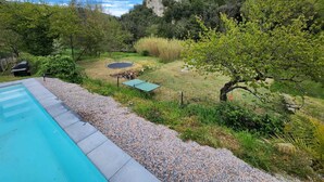 A backyard with a swimming pool, a trampoline, and a fenced area with trees and shrubs. - Villa with swimming pool and private river (Prémian)