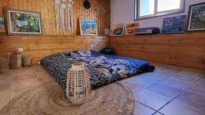 A room with wooden panel walls, a bed with patterned bedding, a woven rug, and wall decorations including framed pictures and dreamcatchers. - Villa with swimming pool and private river (Prémian)