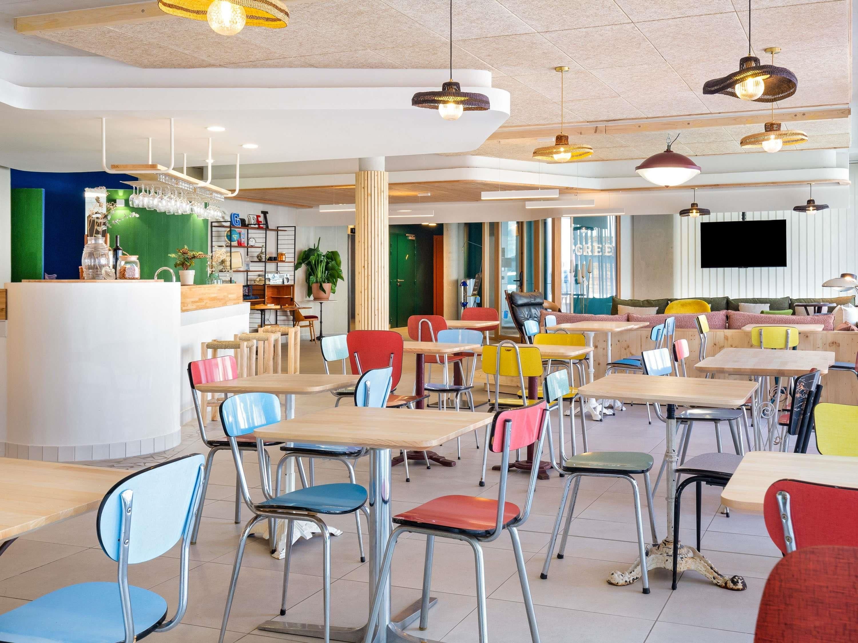 A modern cafe with multiple seating areas, including tables and chairs, and a counter with a variety of items.