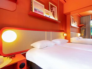 Habitación de hotel con dos camas, una pared roja y un cuadro enmarcado sobre las camas.