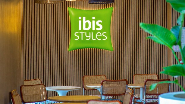 A restaurant interior with a green sign, wooden panel wall, and variously colored chairs and tables. - ibis Styles Salon de Provence (Salon-de-Provence)