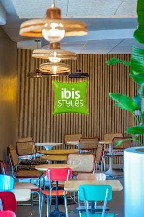Interior de un restaurante con un letrero verde, pared de paneles de madera y sillas y mesas de colores variados.