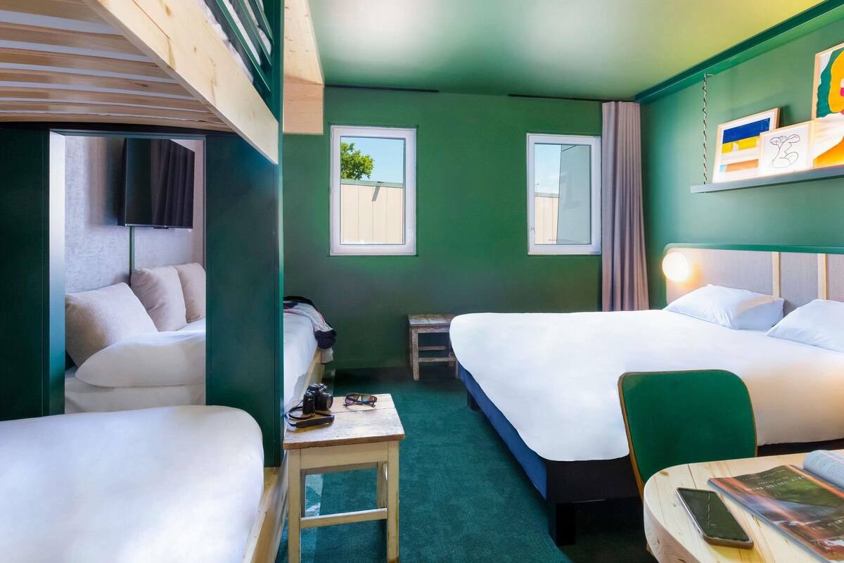A hotel room with two beds, a small table, a chair, a TV, and a window.