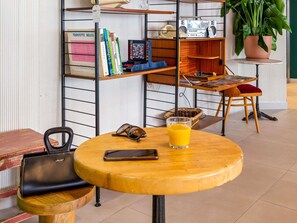 Une table ronde en bois, sur laquelle se trouvent un verre de jus d’orange, un téléphone intelligent et une paire de lunettes de soleil.