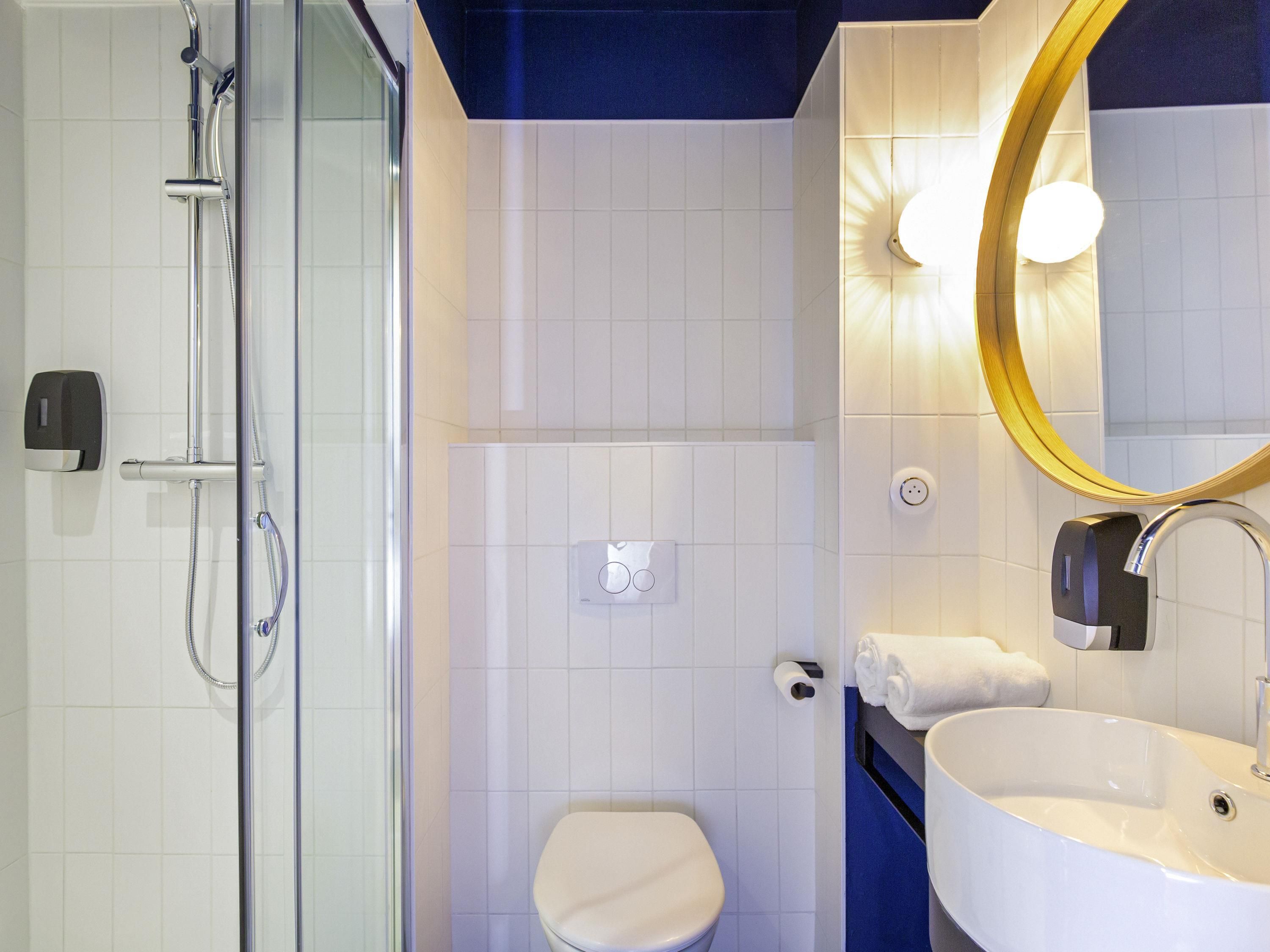 A bathroom with a glass-enclosed shower, a white toilet, a sink with a mirror, and a towel rack.