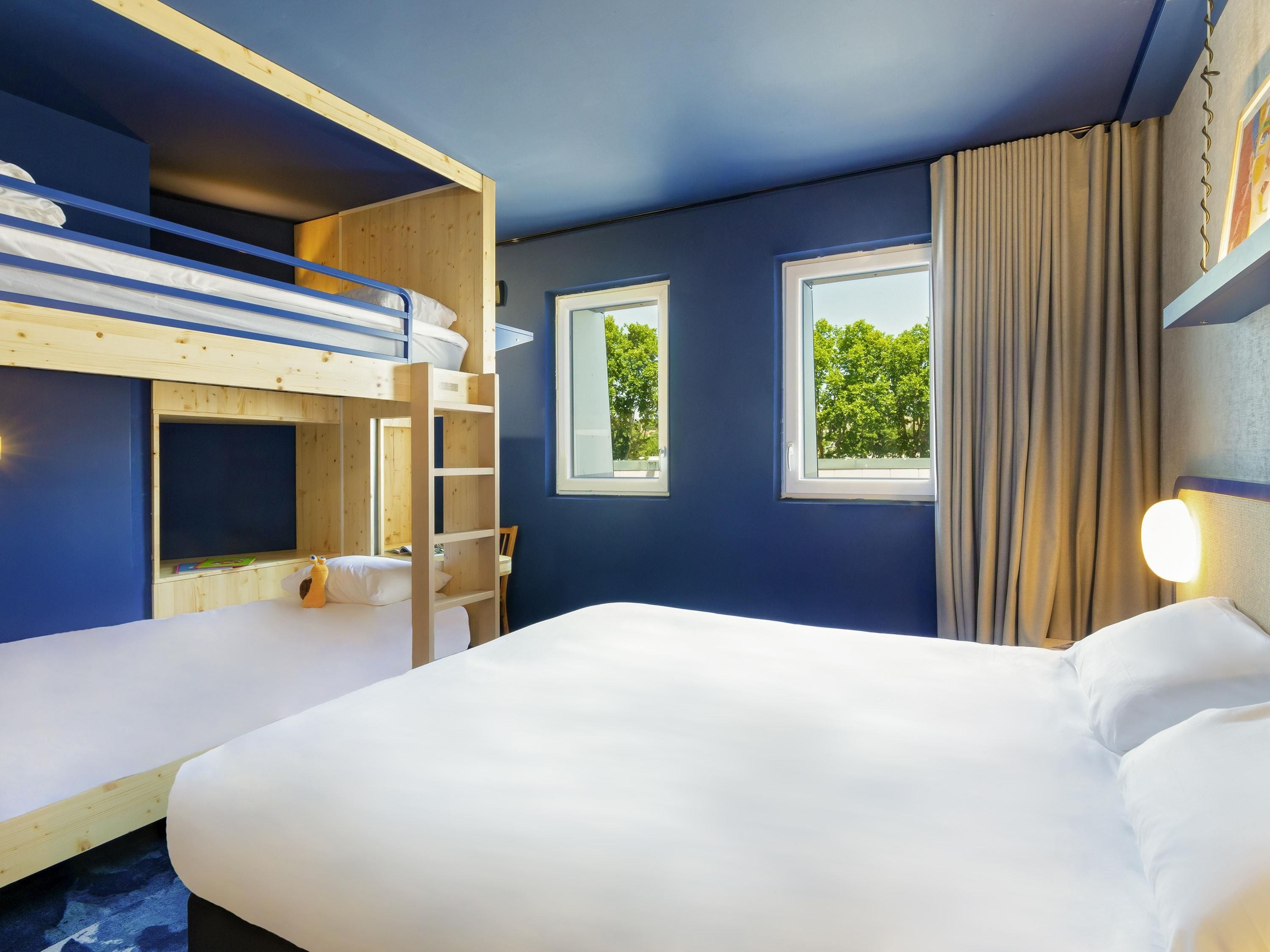 Een kamer met stapelbedden, een groot bed, twee ramen en uitzicht op groen.