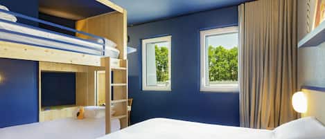 A room with bunk beds, a large bed, two windows, and a view of greenery outside.