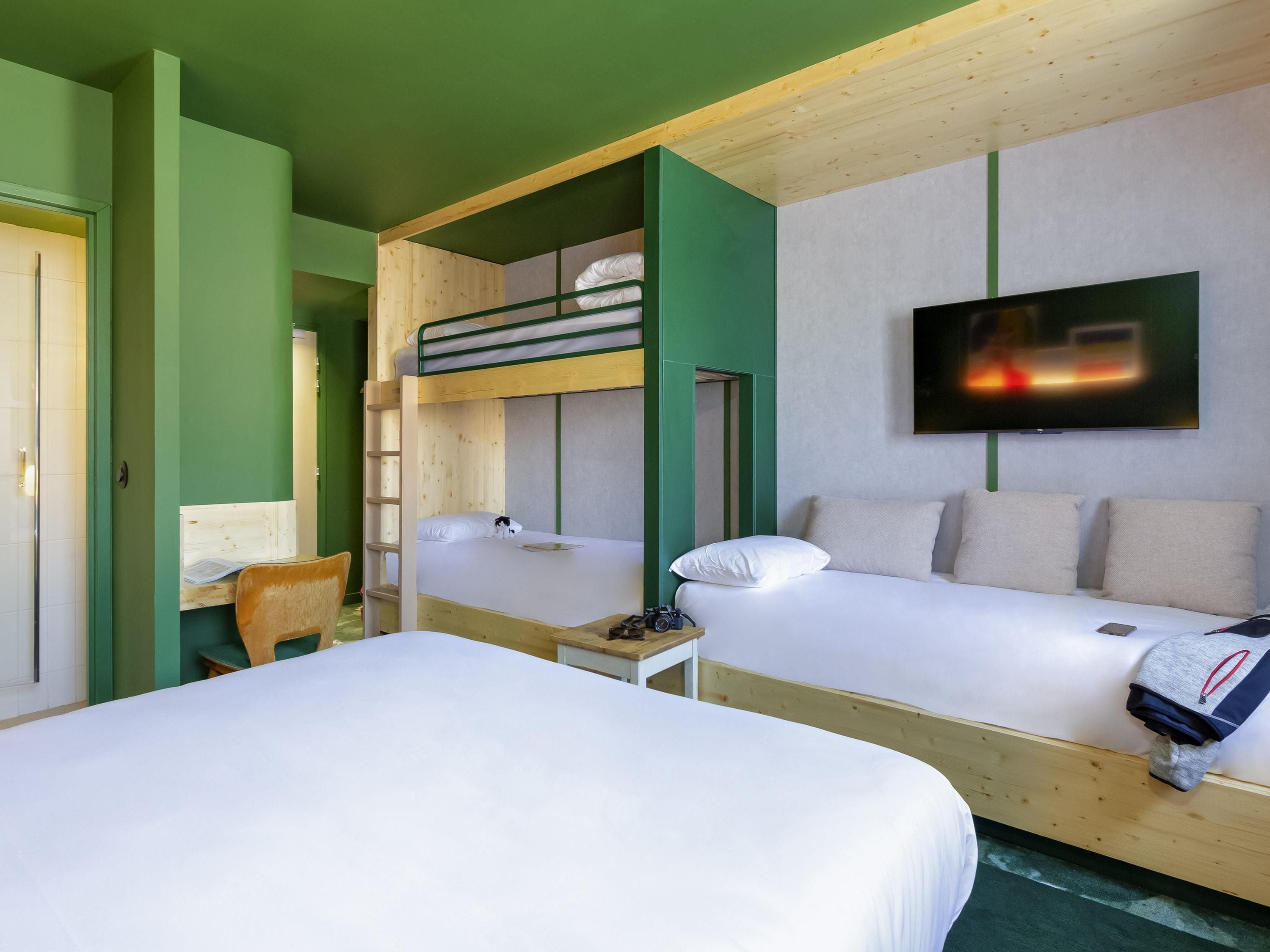 Une chambre avec des lits superposés, un bureau, une chaise, un téléviseur et un lit avec un sac à dos.