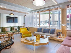Un salon moderne comprenant un canapé, un fauteuil jaune, une table basse et un téléviseur fixé au mur.