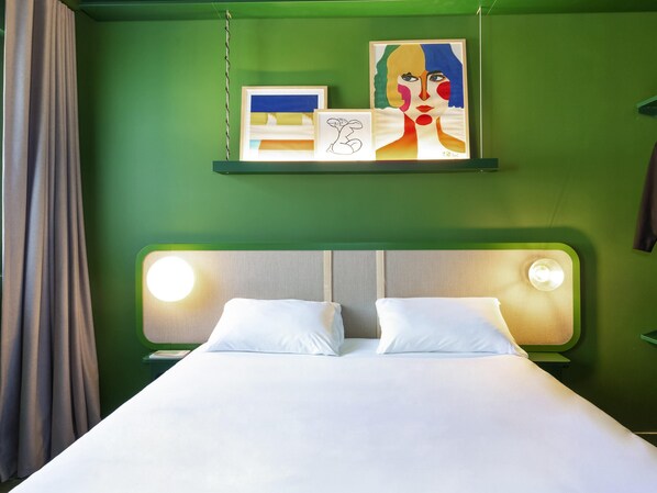 Habitación de hotel con pared verde, cama con ropa blanca, dos lámparas de noche y una obra de arte sobre la cama.
