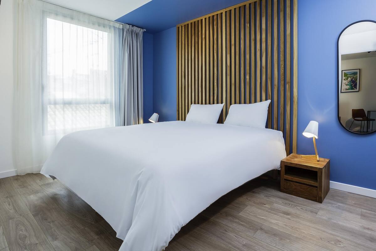 Ein modernes Hotelzimmer mit einem großen Bett, einer Wand aus Holzpaneelen und einem Nachttisch mit einer Lampe.