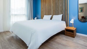 Una habitación de hotel con una cama grande, un cabecero de madera, una mesita de noche con lámpara y un espejo grande en la pared.