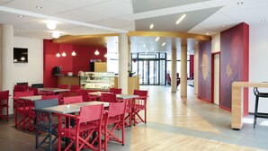 Un restaurant moderne avec des chaises et des tables rouges, un comptoir avec une vitrine, et un intérieur lumineux agrémenté de luminaires au plafond.