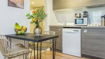 Une cuisine moderne équipée d’un four à micro-ondes, d’une cuisinière et d’un lave-vaisselle. On y trouve une table à manger avec des chaises et un vase rempli de fleurs.