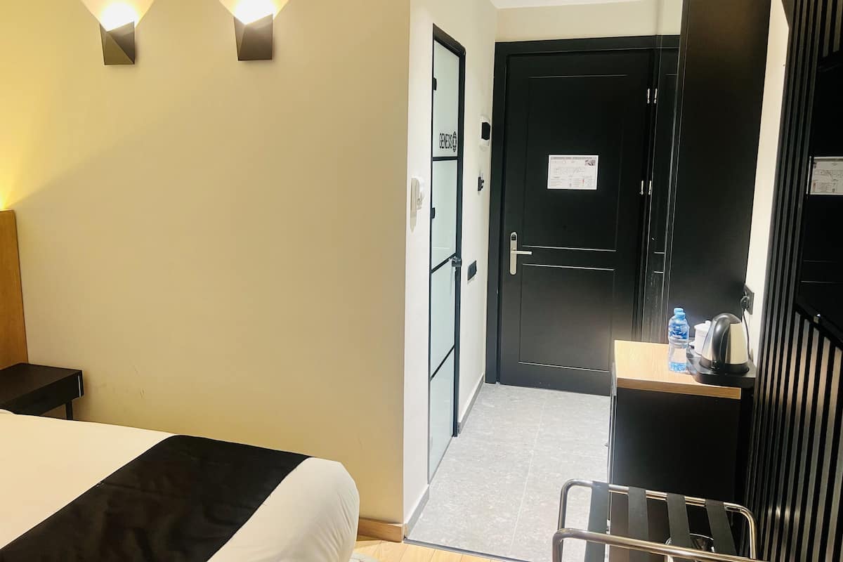 A hotel room with a bed, a desk, a chair, and a door.
