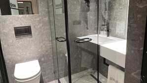 A modern bathroom with a glass-enclosed shower, a toilet, and a sink with a Genesis towel. - Genesis (Tbilisi)