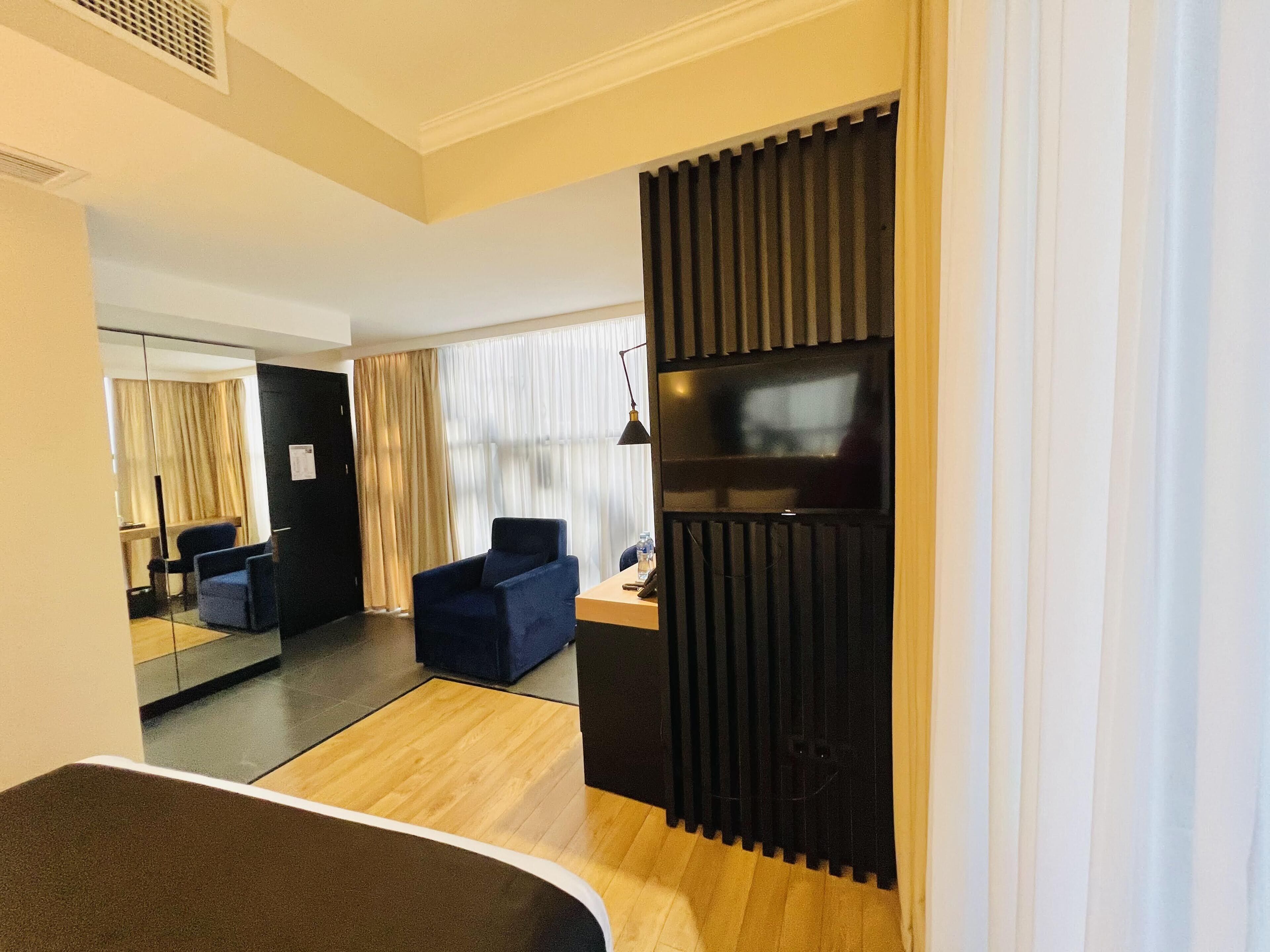 Une chambre d’hôtel moderne avec un plancher en bois, un séparateur noir, une télévision et un coin salon comprenant une chaise et une table.