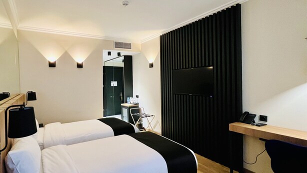 A hotel room with two beds, a desk, a chair, a TV, and a small kitchenette. - Genesis (Tbilisi)