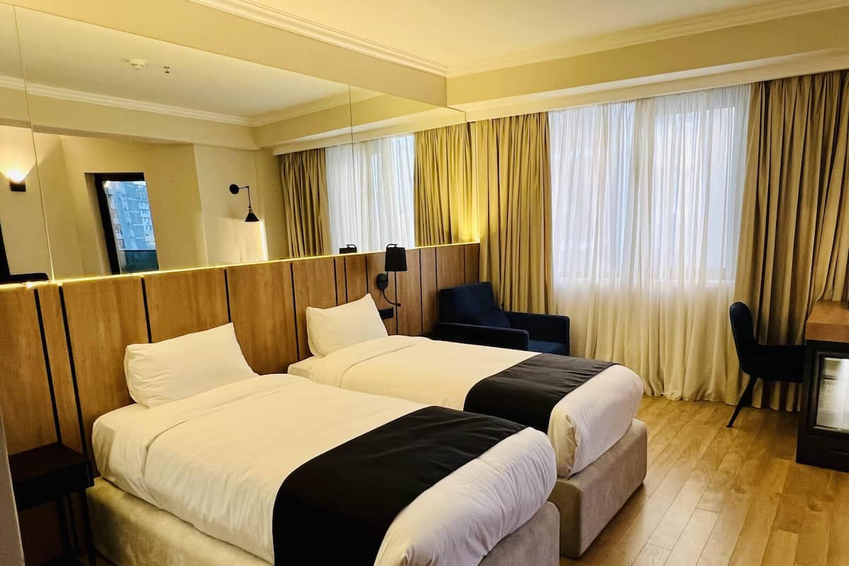 A hotel room with two beds, a desk, a chair, and a large mirror.