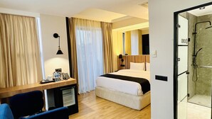 A hotel room with a bed, a desk with a computer, a chair, and a shower area. - Genesis (Tbilisi)