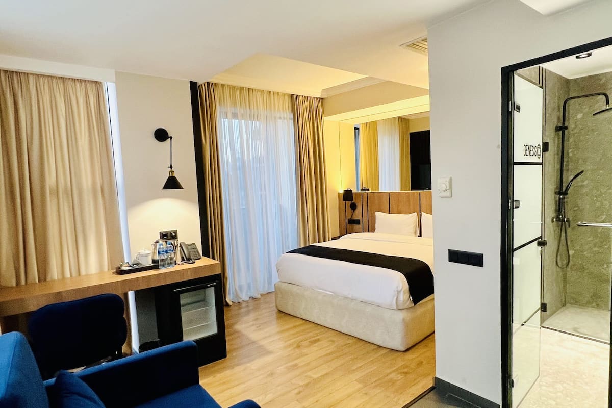 A hotel room with a bed, a desk with a computer, a chair, and a shower area.