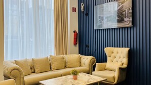 A modern living room with a beige sofa, a matching armchair, and a marble coffee table. A blue accent wall with vertical lines and a mounted television is visible. - Genesis (Tbilisi)