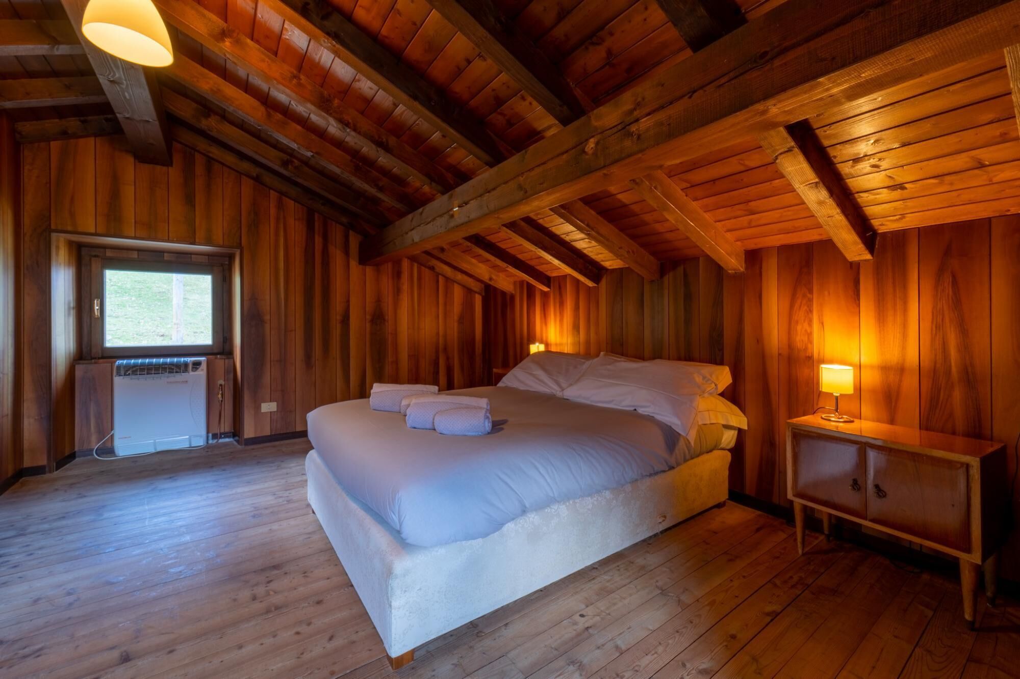 A wooden cabin bedroom with a bed, a nightstand, and a window.