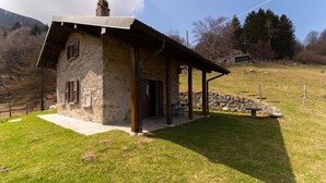 Ein rustikales Steinhaus mit geneigtem Dach und Schornstein, das eine überdachte Außenbereich-Sitzgelegenheit mit Stühlen bietet.