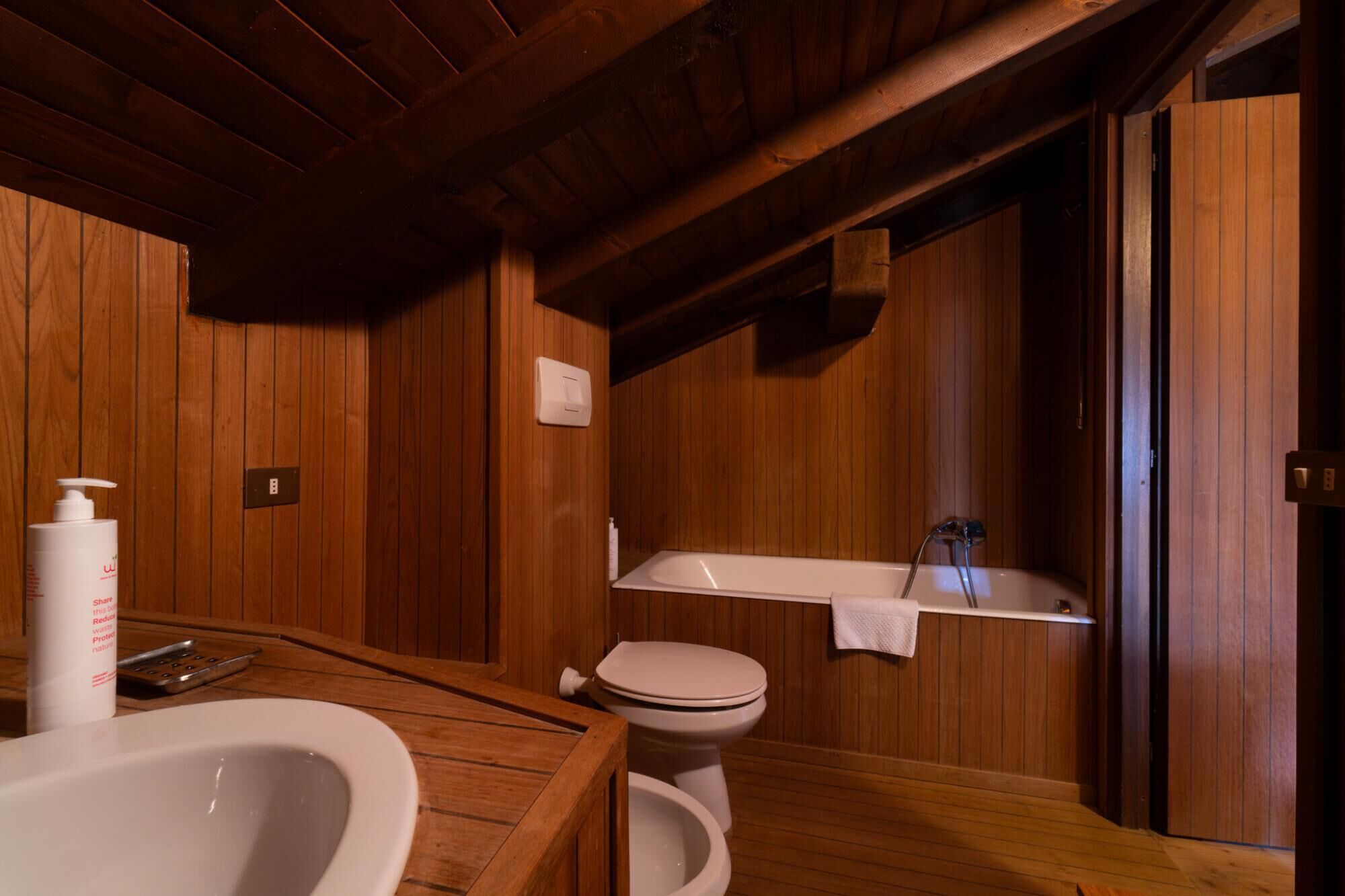 Un baño de madera con bañera, inodoro y lavamanos.
