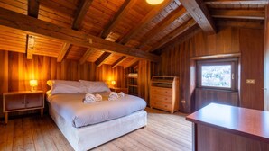 Ein Schlafzimmer einer Holzhütte mit einem Bett, zwei Nachttischen, einem Schminktisch und einem Fenster.