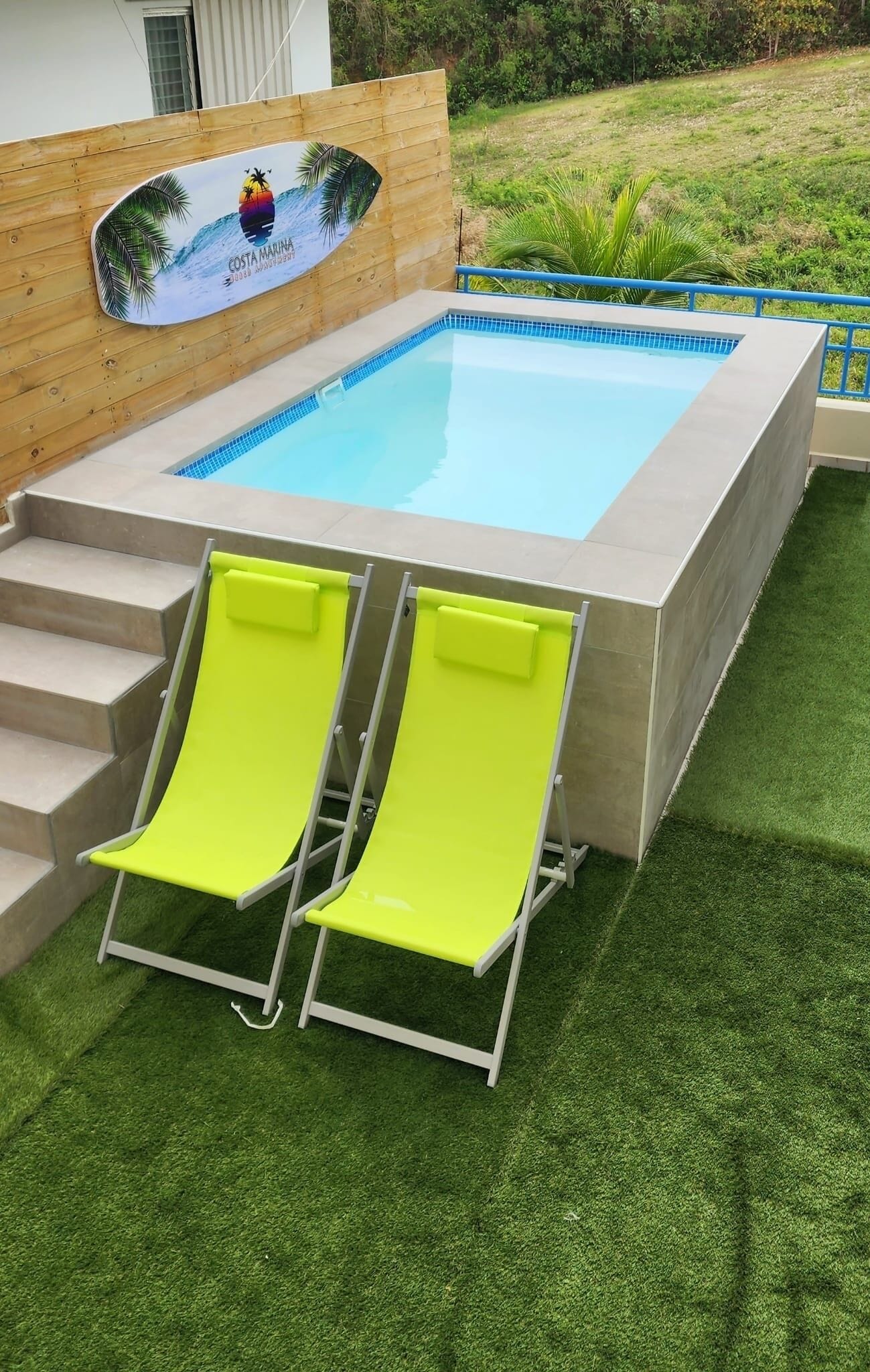 A rectangular pool with a wooden deck and two bright green lounge chairs.