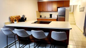 Cozinha com ilha central, banquetas, armários de madeira, geladeira de aço inoxidável e micro-ondas.