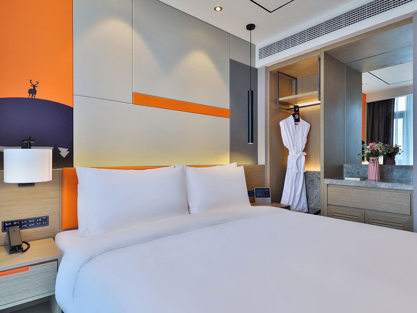 Una habitación de hotel con una cama grande, una bata colgada en la puerta, una mesita de noche con una lámpara y un espejo.