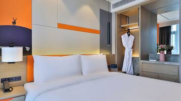 Una habitación de hotel con una cama grande, una bata colgada en la puerta, una mesita de noche con una lámpara y un espejo.